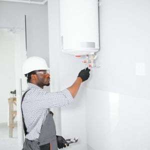 Young African Male Plumber Repairing Boiler.